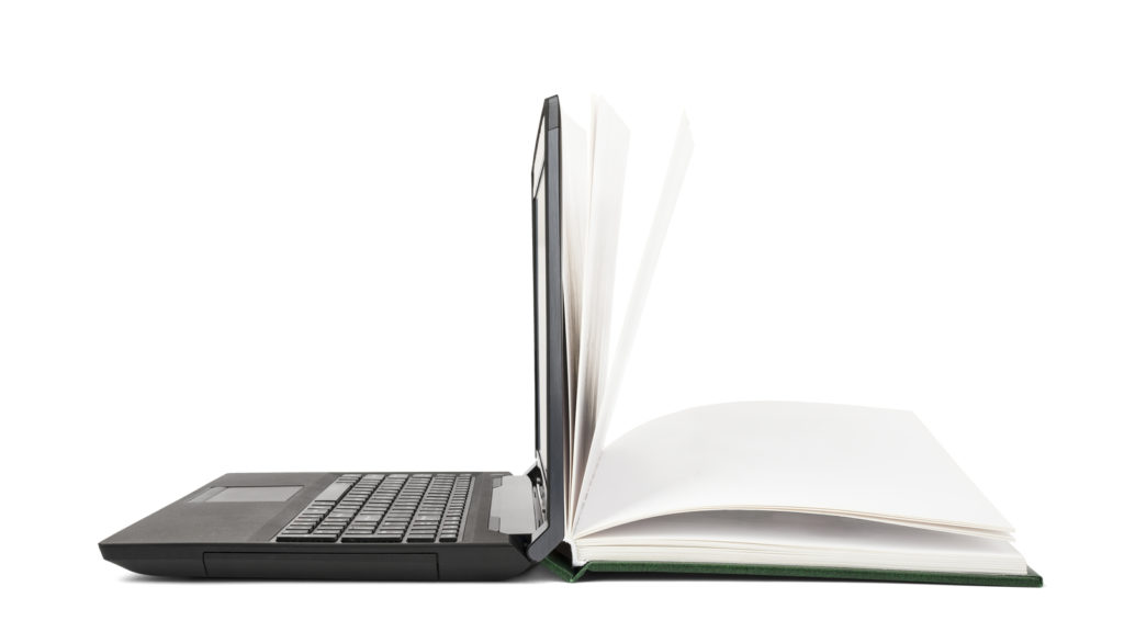 The image shows a laptop and a textbook opened next to each other, leaning back to back to each other to signify how has technology changed from the past to the present.
